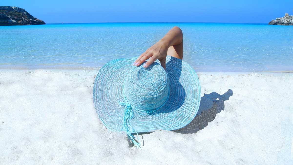 woman in a blue hat sitting on the sand by the ocean