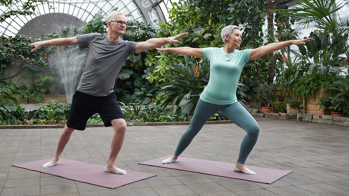 mature man and woman doing yoga surrounded by plants
